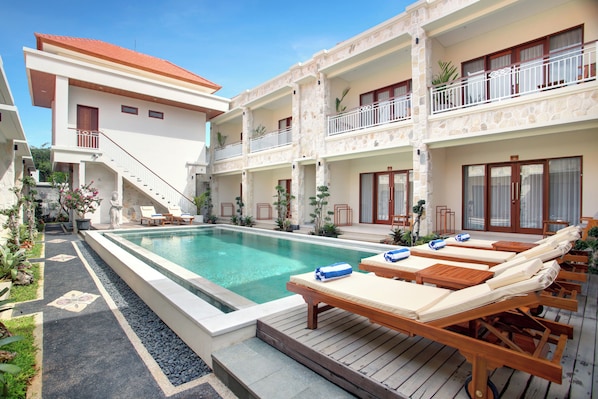 A hotel with a swimming pool, lounge chairs, and a staircase leading to the upper floors.
