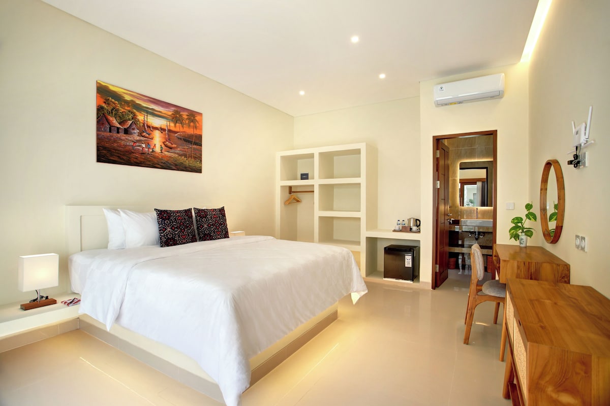 A modern hotel room with a large bed, a desk, a mirror, and a painting on the wall.