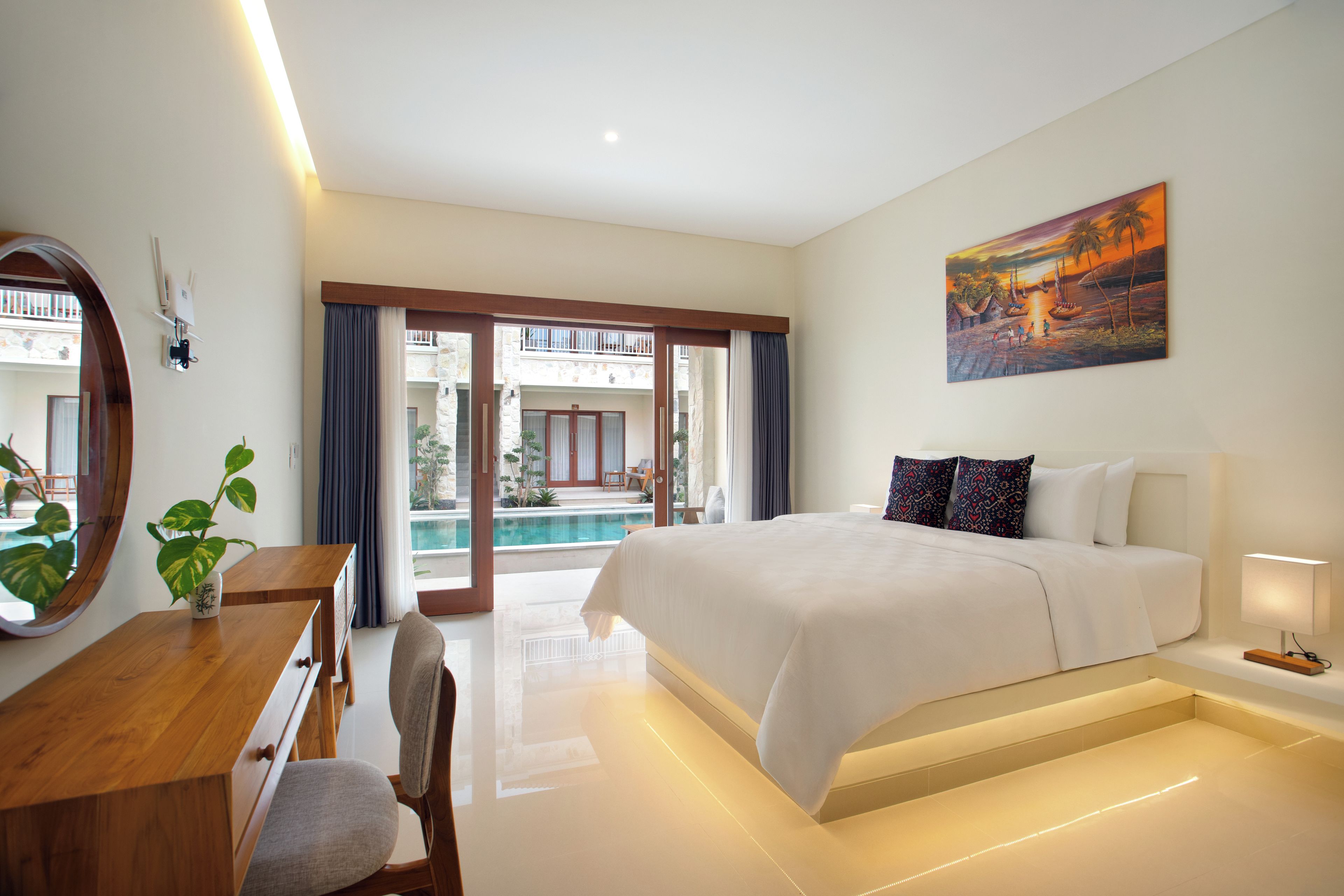 Una habitación de hotel moderna con una cama grande, un escritorio, una silla, una planta en maceta y vistas a una piscina y zona exterior.
