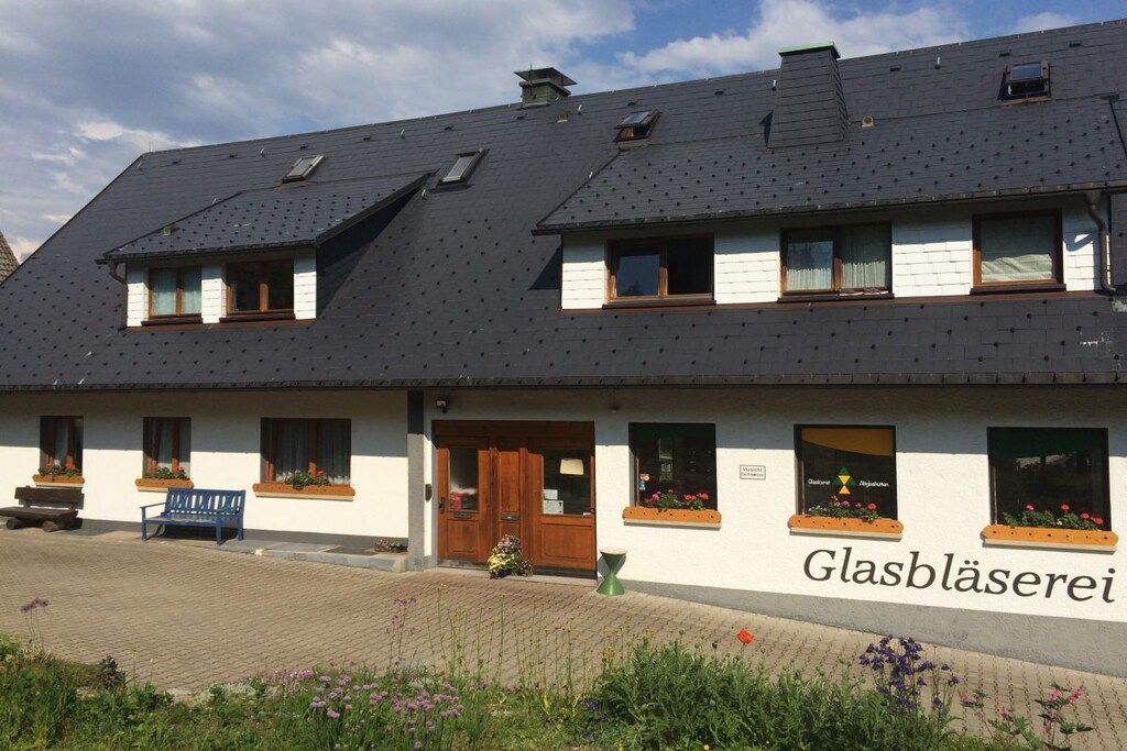 Un bâtiment à deux étages, doté d’un toit en pente, de nombreuses fenêtres et d’une enseigne sur laquelle on peut lire « Glasbläserrei ».