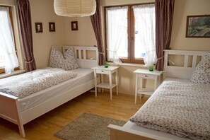 Ein Schlafzimmer mit zwei Einzelbetten, einem kleinen Schreibtisch und einem Fenster mit Vorhängen.