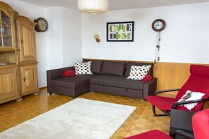 Ein Wohnzimmer mit einem Ecksofa, einem roten Sessel, einer Holzkommode und einer Wanduhr.