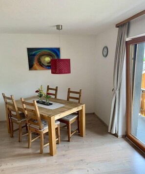 Ein Essbereich mit Holztisch und Stühlen, einem Bild an der Wand und einem Fenster mit Vorhängen.