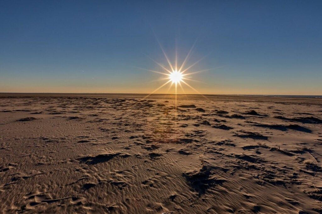 Una playa con huellas y el sol cerca del horizonte.
