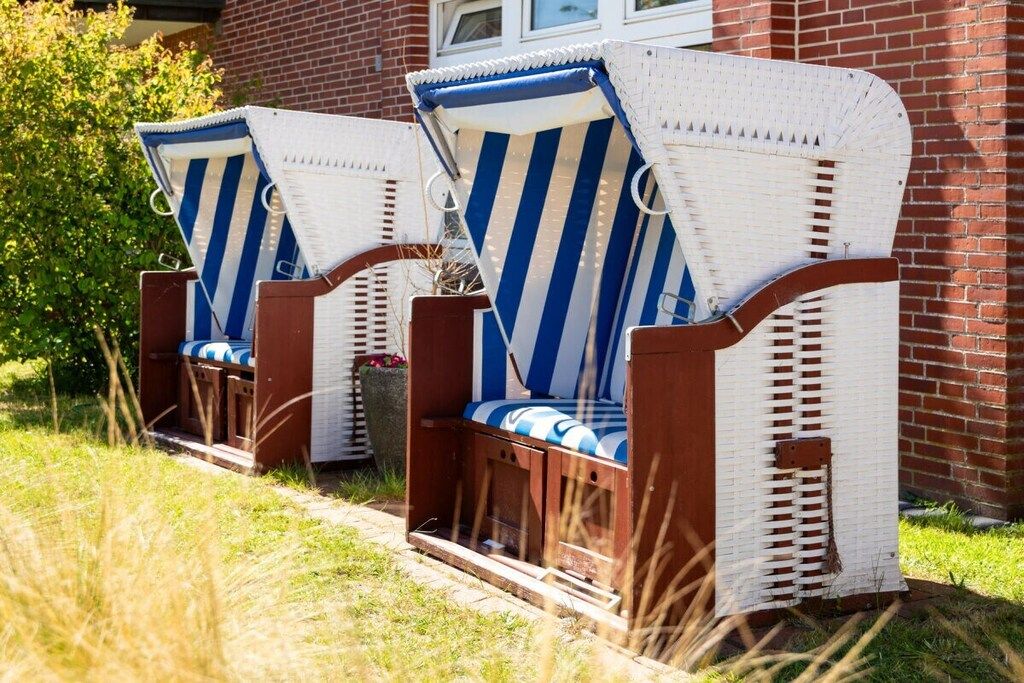 Two wicker lounge chairs with blue and white stripes, positioned on a grassy area in front of a brick building.