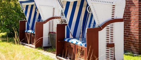 Two wicker lounge chairs with blue and white stripes, positioned on a grassy area in front of a brick building.