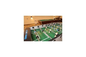 Une table de baby-foot dans une pièce où se trouvent également une table de billard et un canapé.