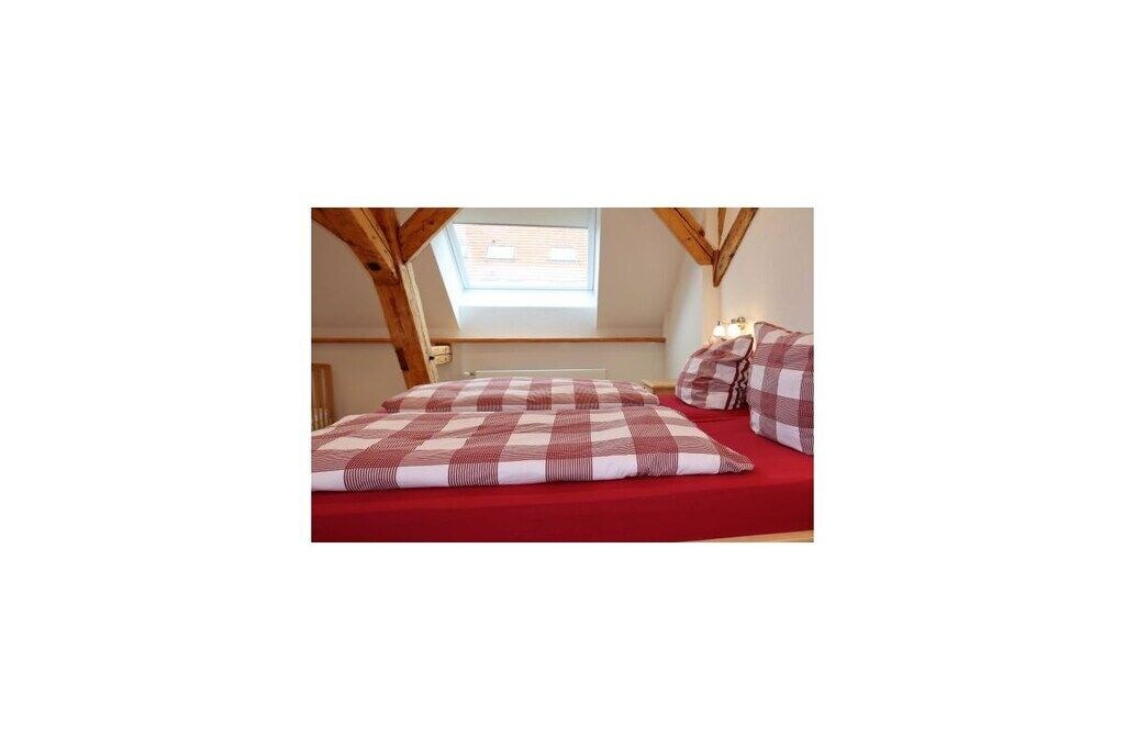 A bedroom with a sloped ceiling, a window, and a bed with checkered bedding.