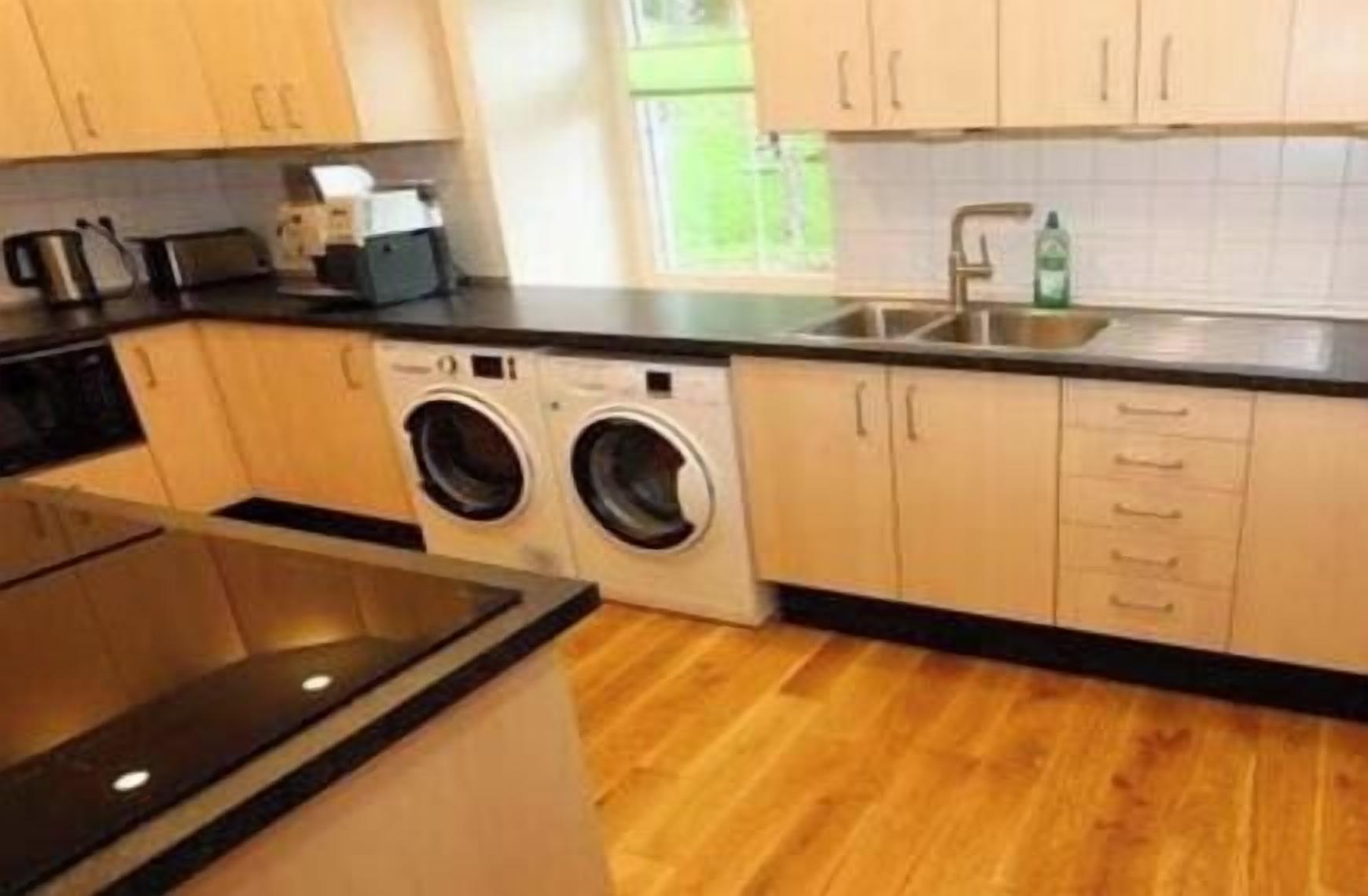 Une cuisine équipée d’un lave-linge, d’un évier et de meubles de rangement en bois.