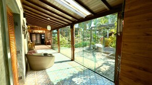 Una habitación tradicional japonesa con suelo de tatami, techo de madera bajo y una puerta corredera de vidrio que da a un jardín exterior.