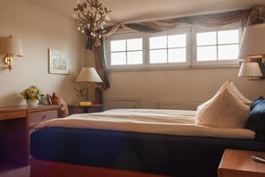 Een hotelkamer met een groot bed, twee bedlampen, een raam met gordijnen, een kleine tafel met een bloevas en een schilderij aan de muur.