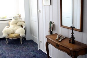 Een kamer met een zachte witte teddybeer op een stoel, een houten console tafel met een spiegel, en een raam met uitzicht.