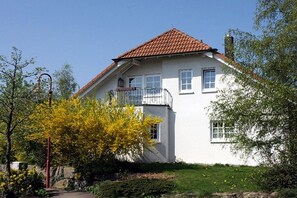 Een herenhuis met een rode pannendak, witte buitenmuren en een klein balkon op de tweede verdieping.