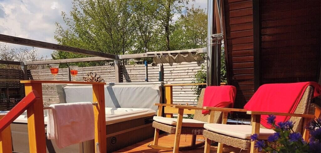Eine Terrasss mit Holz-Pergola, einem Sofa, zwei Korbstühlen mit roten Kissen und einem kleinen Tisch.