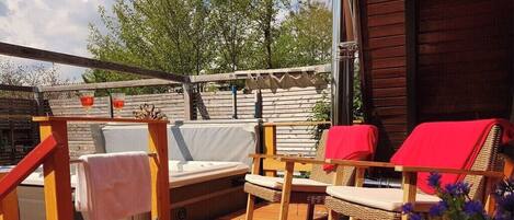 Eine Terrasss mit Holz-Pergola, einem Sofa, zwei Korbstühlen mit roten Kissen und einem kleinen Tisch.