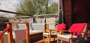 Eine Terrasss mit Holz-Pergola, einem Sofa, zwei Korbstühlen mit roten Kissen und einem kleinen Tisch.