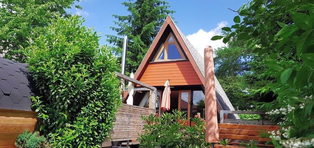 A wooden cabin with a triangular roof, surrounded by lush greenery.