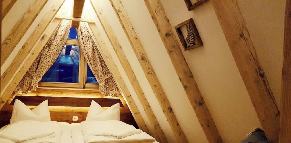 Une chambre avec un plafond en pente, une fenêtre avec des rideaux et un lit avec des oreillers.