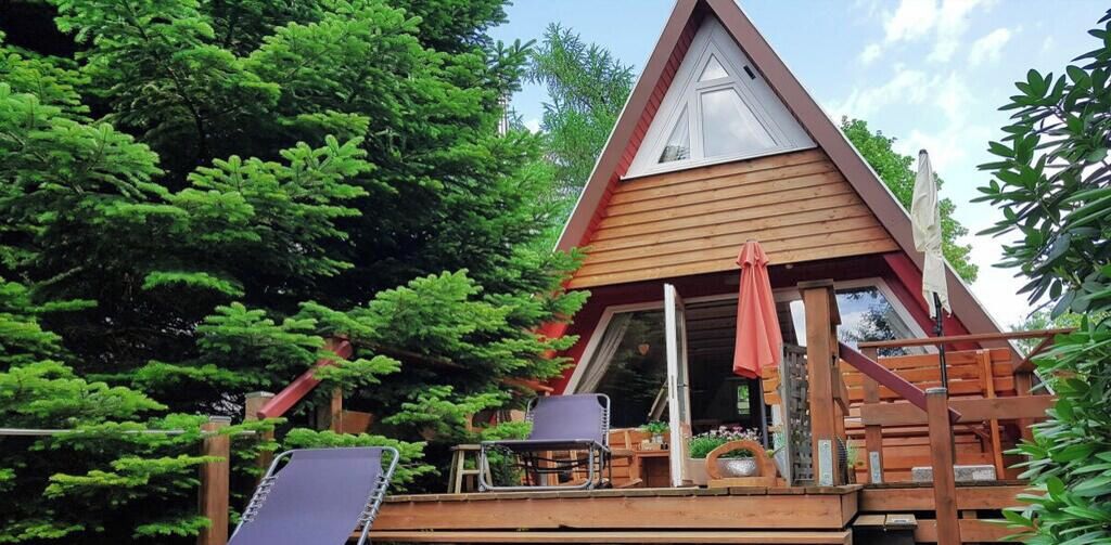 A wooden cabin with a triangular roof, a deck with chairs, and a large window.