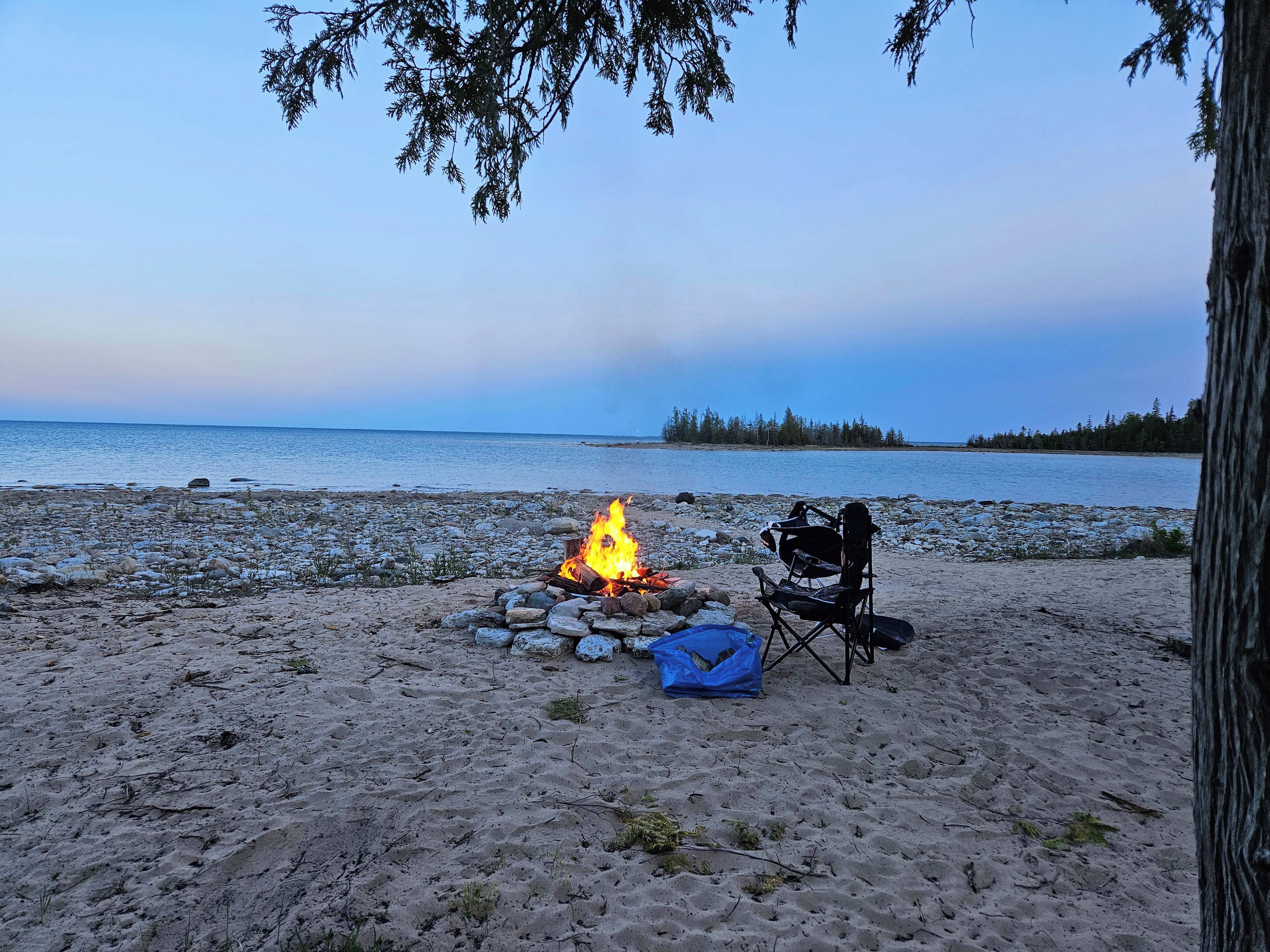 Une scène de plage avec un feu de camp, une chaise et un sac.