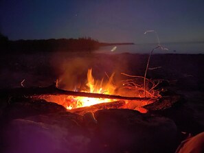A campfire with visible flames and embers, surrounded by rocks and a dark sky. - Soothing 3 Arce private campground on Lake Huron in lovely De Tour Village (De Tour Village)