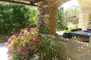 Une structure en pierre comprenant une table et des chaises, entourée de verdure et de plantes en fleurs.