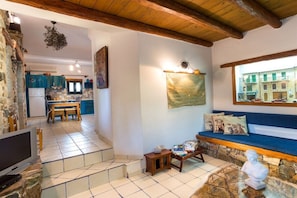 Un intérieur chaleureux avec un mur en pierre, un plafond en bois, un coin repas et un espace salon offrant une vue sur les bâtiments environnants.