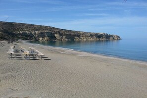 A beach with a row of sunbeds and umbrellas. - Villa in Pitsidia with swimming pool (Pitsidia)
