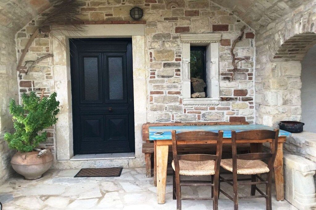 A stone-walled room with a black door, a small window, and a wooden table with chairs.