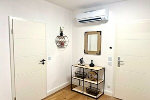 A hallway with white doors, a wall-mounted air conditioner, a small shelf with decorative items, and a mirror. - Holiday apartment with 1 bedroom (Landau in der Pfalz)
