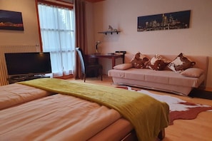 Une chambre d’hôtel avec un lit, un canapé, une télévision, un bureau et un tableau représentant un paysage urbain.