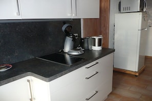 Cuina amb taulell negre, armaris blancs, cafetera i nevera blanca.