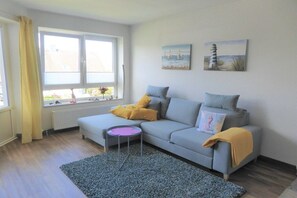 Ein modernes Wohnzimmer mit einem grauen Sofa, einem kleinen Beistelltisch und einem Fenster mit Vorhängen.