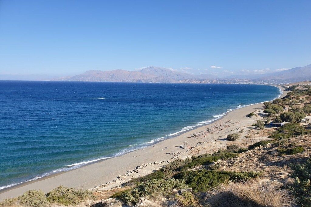 A coastal landscape with a beach, clear sky, and distant mountains.