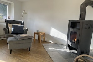 Ein Wohnzimmer mit grauem Sofa, einem kleinen Holztisch, einer Lampe und einem Kaminofen.