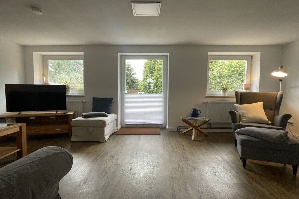 Ein Wohnzimmer mit Fernseher, Sofa, Sessel und einem kleinen Tisch mit Lampe.