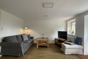 Ein Wohnzimmer mit einer Couch, einem Couchtisch, einem Fernseher und einem Fenster.