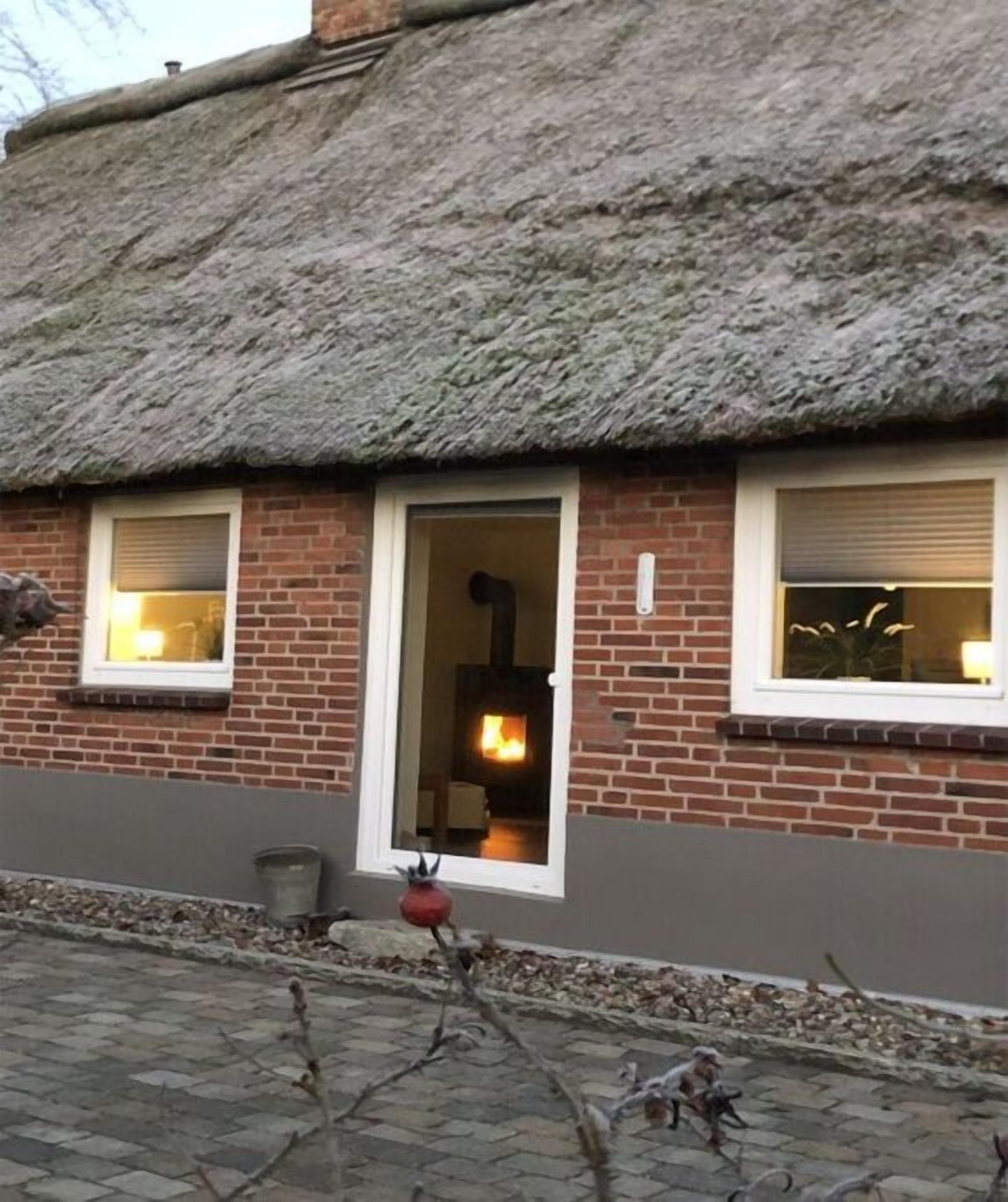 A brick building with a thatched roof, a visible fireplace, and a window with a closed shutter.