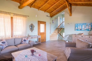 A spacious living room with a wooden ceiling, a staircase, and a painting of sailboats.