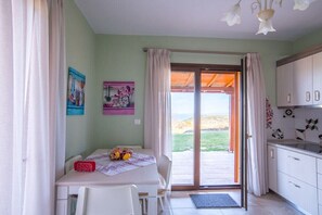 A room with a dining table, chairs, a kitchen area, and a sliding glass door leading to an outdoor area.