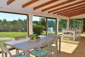 An open-plan dining area with a table set for four, large windows, and a view of the outdoors.