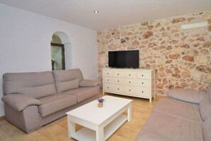 A living room with a beige sofa, a white coffee table, a TV on a stone wall, and a white cabinet.