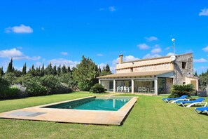 A house with a swimming pool, outdoor seating, and a stone facade.
