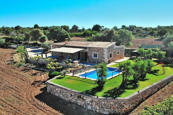 A stone villa with a swimming pool, surrounded by a well-maintained garden and olive trees.