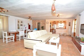A spacious living area with a sofa, dining table, and chairs, a kitchen in the background, and a TV mounted on the wall. - Cabin with 1 bedroom (Santa Margalida)