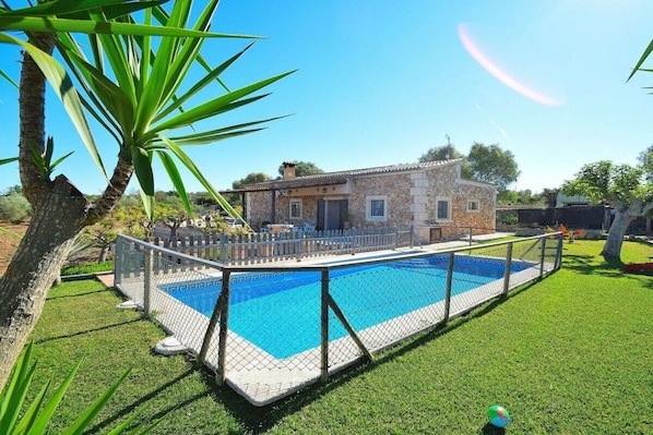 A residential property with a swimming pool, a fenced yard, and a stone building.
