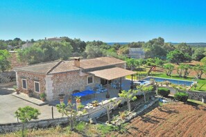 Une maison en pierre avec un toit en tuiles, une terrasse avec des meubles d’extérieur et une piscine.