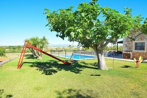 Un jardin avec une balançoire, un arbre, une piscine et une maison en pierre.
