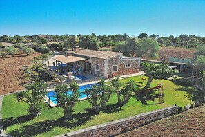 A two-story stone house with a swimming pool, surrounded by a well-maintained lawn and trees.