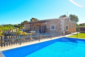 A stone house with a swimming pool, a wooden fence, and a clear blue sky.